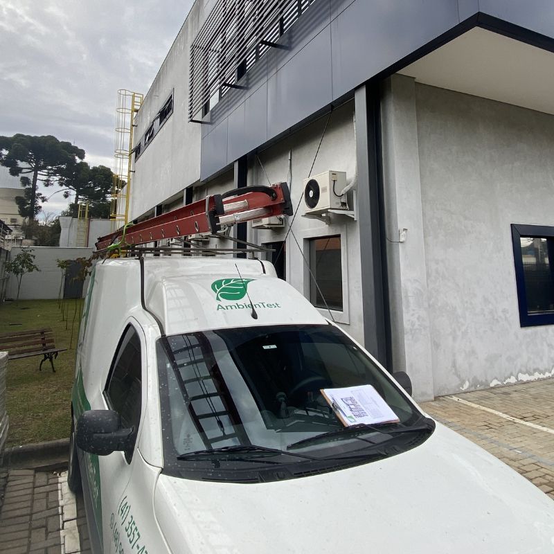 Equipe técnica da Ambientest realizando ensaio de campo em equipamento pesado, profissionais com uniforme e EPIs operando instrumentos de medição, ambiente externo industrial, luz natural diurna, fotografia profissional ultra-realista